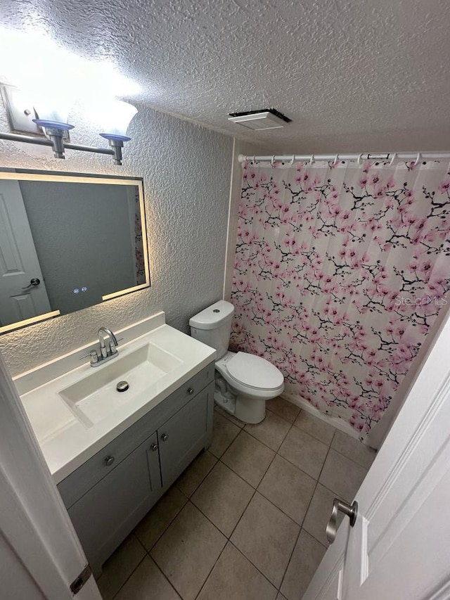 bathroom featuring a textured wall, toilet, a textured ceiling, vanity, and tile patterned floors