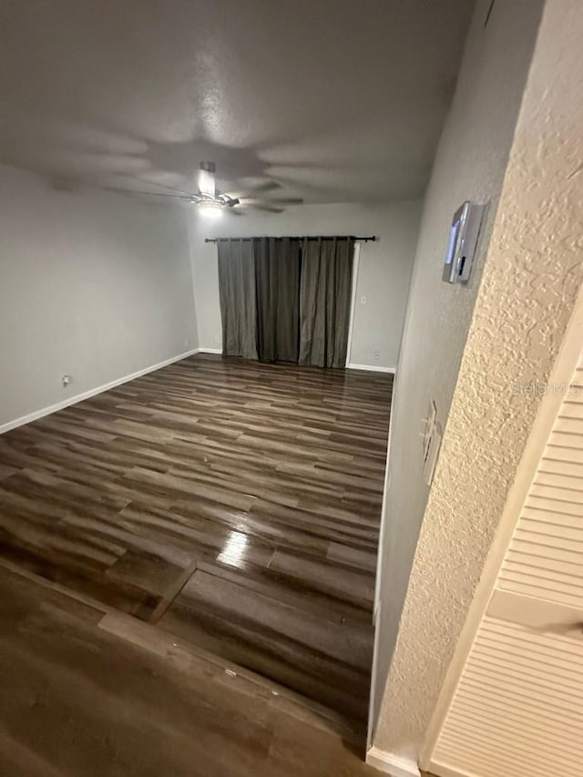 empty room featuring a ceiling fan, dark wood-style flooring, and baseboards