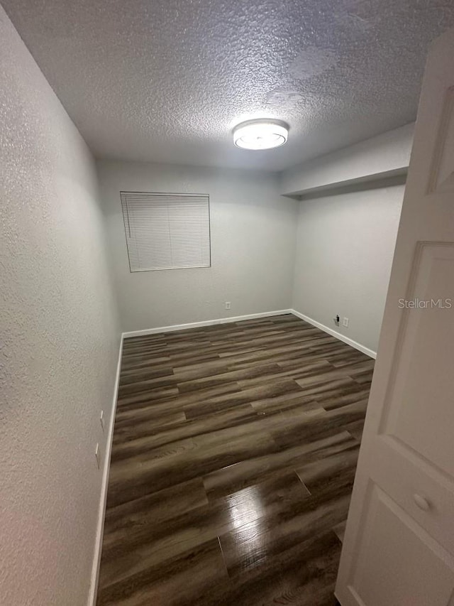 unfurnished room featuring a textured ceiling, a textured wall, dark wood-style flooring, and baseboards