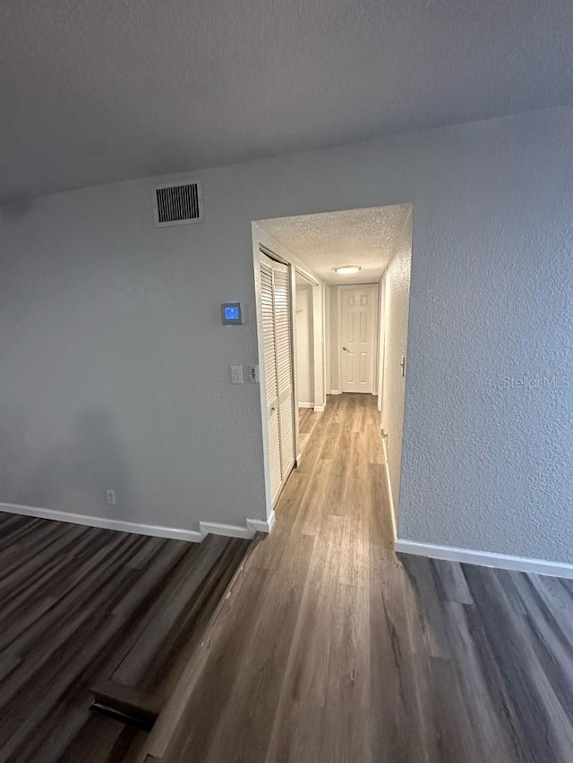 hall with visible vents, a textured ceiling, baseboards, and wood finished floors