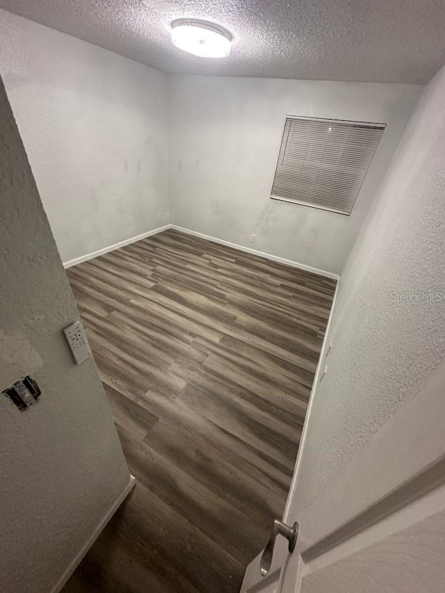 spare room with baseboards, dark wood finished floors, and a textured ceiling