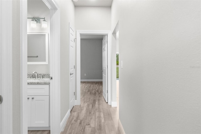 hall featuring a sink, light wood-style flooring, and baseboards