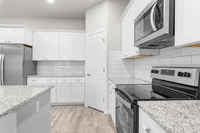 kitchen featuring light wood finished floors, appliances with stainless steel finishes, white cabinets, and light stone counters