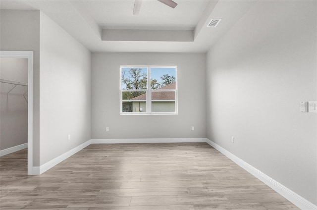 unfurnished bedroom with a raised ceiling, visible vents, baseboards, and light wood finished floors