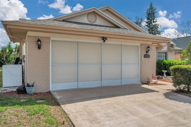 exterior space featuring driveway, a shingled roof, a garage, and brick siding