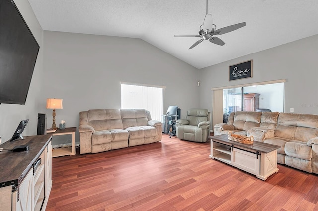 living area with ceiling fan, vaulted ceiling, a textured ceiling, and wood finished floors