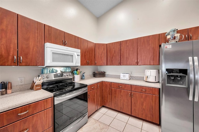 kitchen featuring light countertops, appliances with stainless steel finishes, light tile patterned flooring, and a towering ceiling