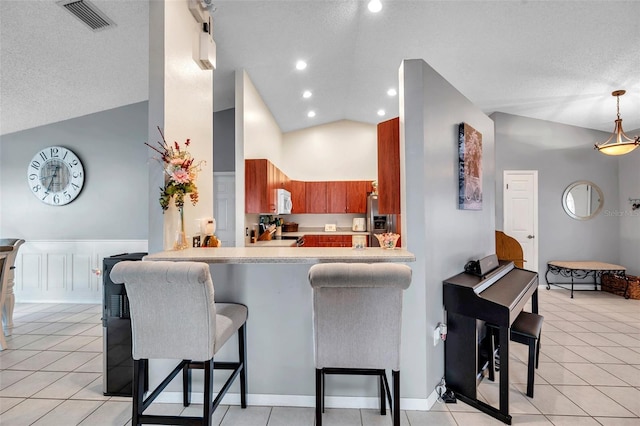 kitchen featuring visible vents, lofted ceiling, a breakfast bar, a peninsula, and light countertops