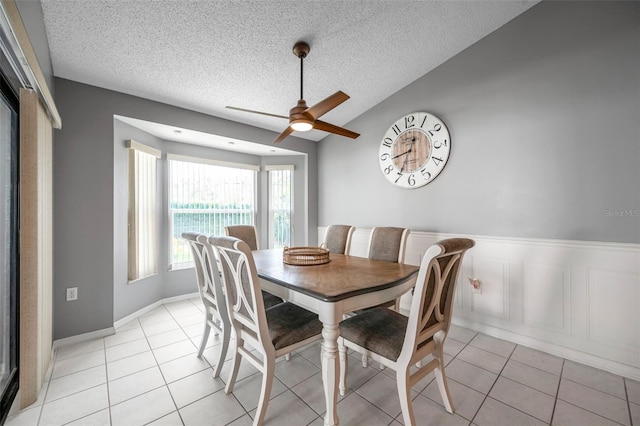 dining space with vaulted ceiling, a textured ceiling, light tile patterned flooring, and a wainscoted wall