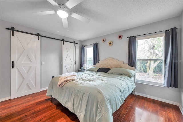 bedroom with dark wood-style floors, a barn door, and baseboards