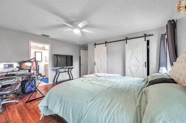 bedroom featuring a textured ceiling, a barn door, dark wood-style flooring, visible vents, and a ceiling fan