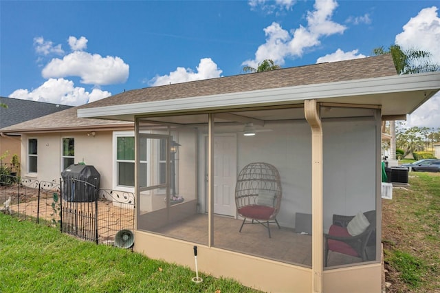 back of house featuring a sunroom, a shingled roof, central AC unit, and stucco siding