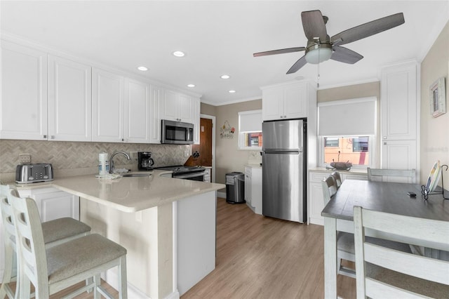 kitchen featuring light countertops, appliances with stainless steel finishes, white cabinetry, a sink, and a peninsula