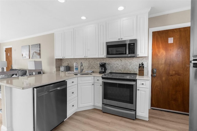 kitchen with light countertops, appliances with stainless steel finishes, ornamental molding, white cabinets, and a peninsula