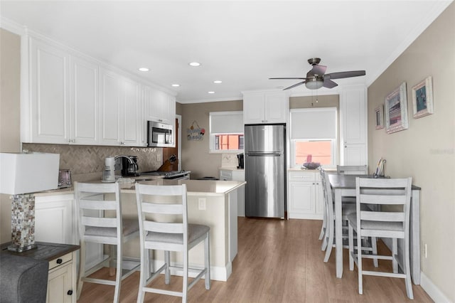 kitchen featuring appliances with stainless steel finishes, white cabinets, decorative backsplash, and a kitchen bar