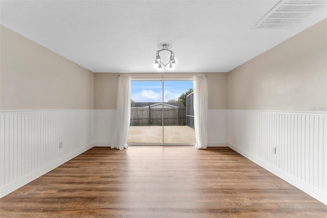 unfurnished dining area with a wainscoted wall, visible vents, and wood finished floors