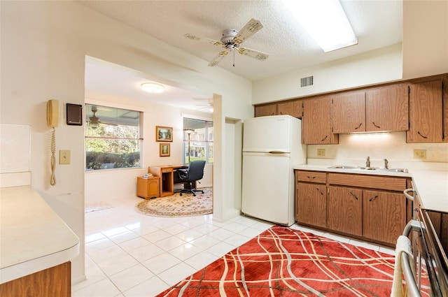 kitchen featuring brown cabinets, light countertops, a ceiling fan, freestanding refrigerator, and a sink