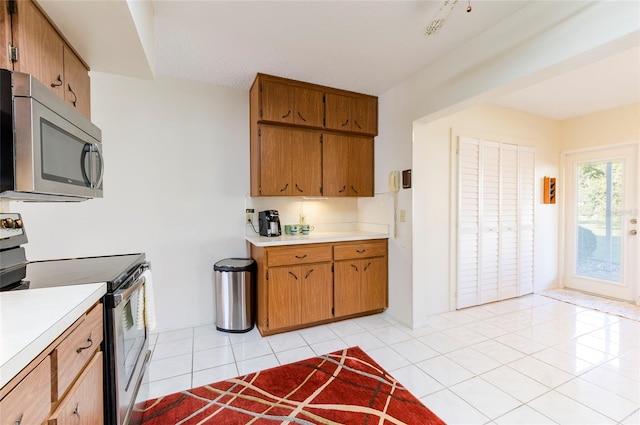 kitchen with appliances with stainless steel finishes, brown cabinetry, light countertops, and light tile patterned floors