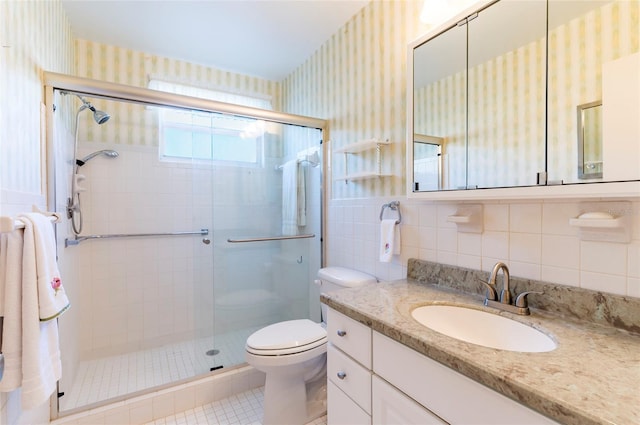 full bathroom with wallpapered walls, toilet, vanity, a shower stall, and tile walls