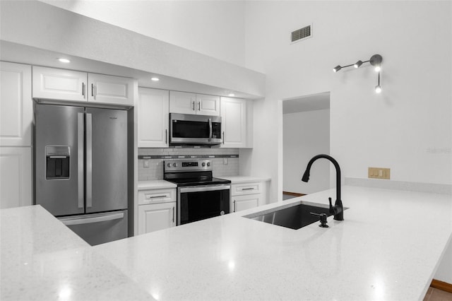 kitchen with light stone counters, stainless steel appliances, a sink, visible vents, and backsplash