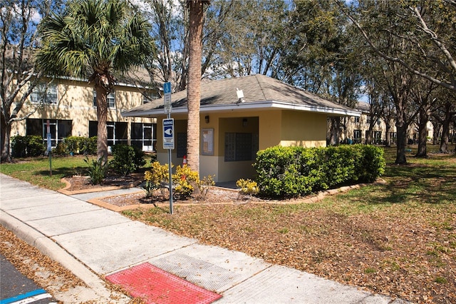 view of front of property featuring a shingled roof, a front lawn, and stucco siding