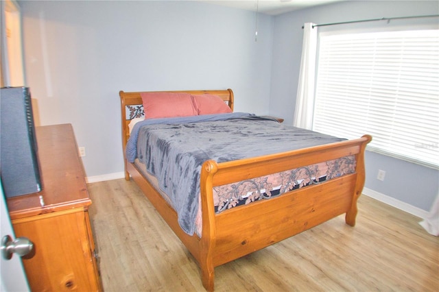 bedroom with baseboards, multiple windows, and light wood-style floors