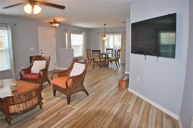 living area with baseboards, ceiling fan, and light wood-style floors