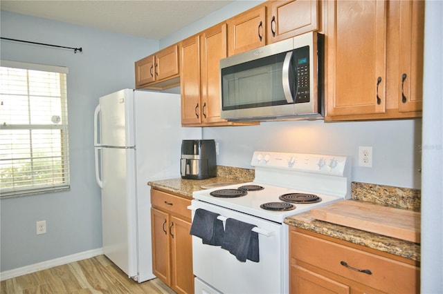 kitchen with brown cabinets, light stone countertops, light wood-type flooring, white appliances, and baseboards