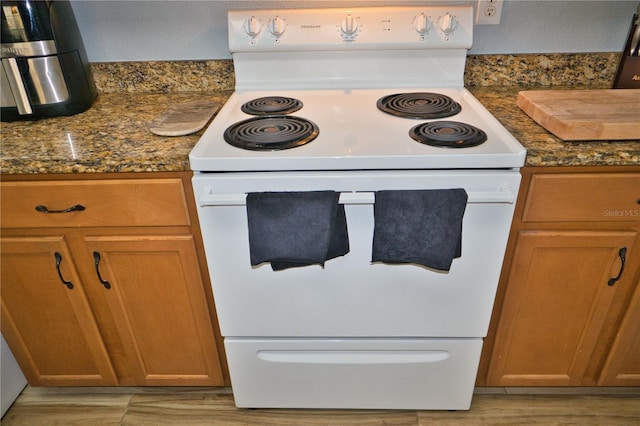 kitchen with brown cabinetry, dark stone counters, white electric stove, and light wood-style flooring