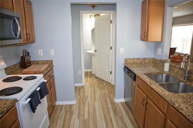 kitchen featuring appliances with stainless steel finishes, wood tiled floor, brown cabinetry, a sink, and dark stone countertops