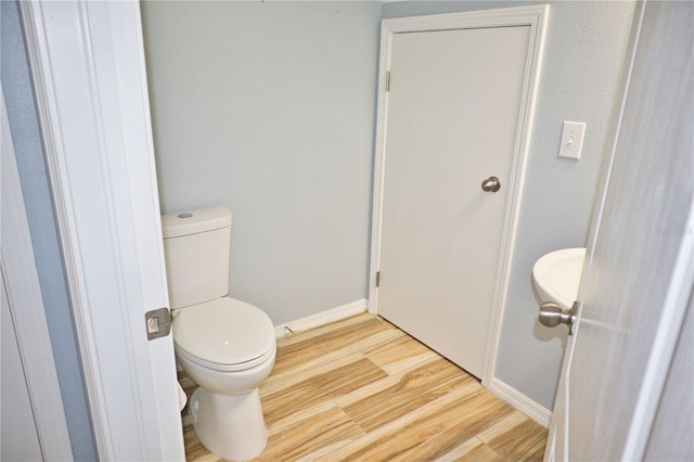 bathroom with toilet, baseboards, and wood finished floors