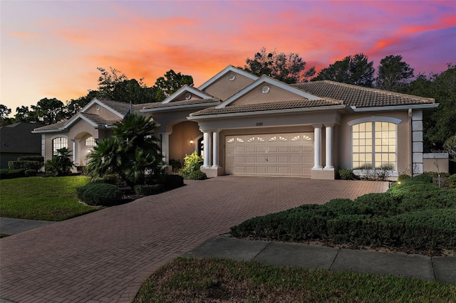 view of front of home featuring an attached garage, a tile roof, decorative driveway, stucco siding, and a front lawn