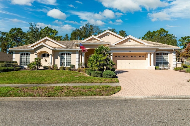 view of front of house with decorative driveway, a tiled roof, an attached garage, and stucco siding