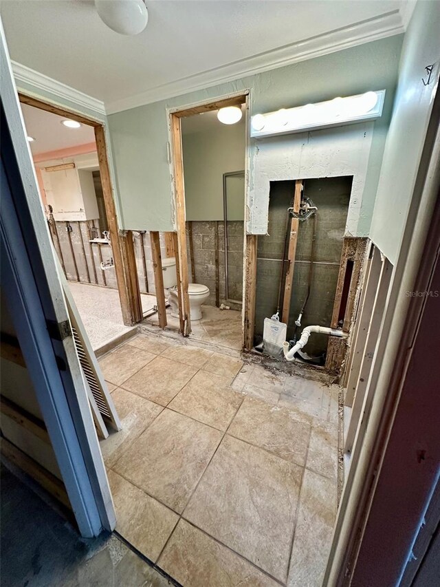 bathroom featuring a wainscoted wall, crown molding, tile walls, and toilet