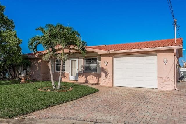 single story home with an attached garage, a tile roof, decorative driveway, stucco siding, and a front lawn