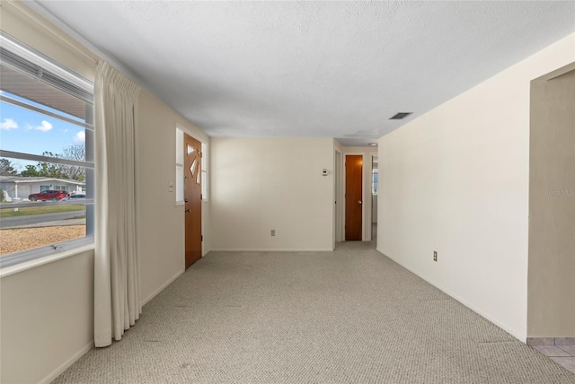 spare room featuring light colored carpet, visible vents, a textured ceiling, and baseboards