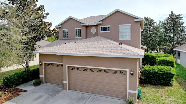 traditional-style home featuring a garage, roof with shingles, concrete driveway, and stucco siding