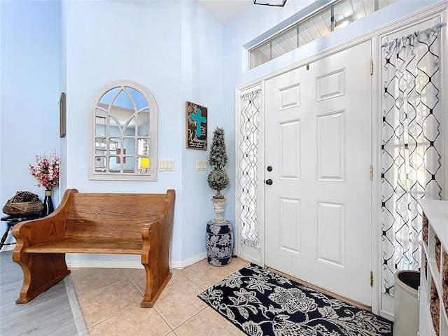 entryway featuring light tile patterned floors, a high ceiling, and baseboards