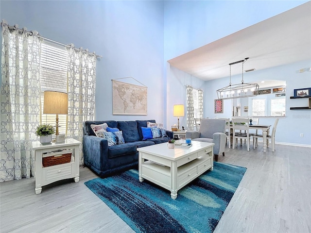 living room with a high ceiling, visible vents, baseboards, and wood finished floors