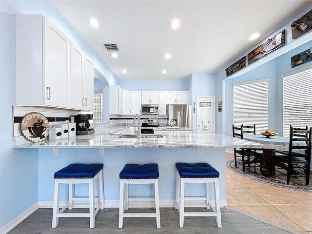 kitchen featuring visible vents, a breakfast bar area, appliances with stainless steel finishes, a peninsula, and a sink