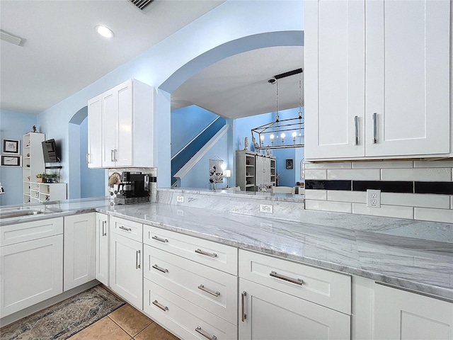 kitchen featuring arched walkways, a sink, white cabinets, light stone countertops, and decorative light fixtures