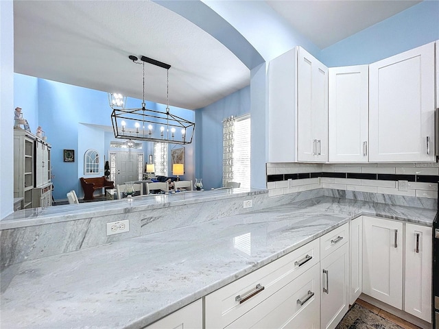 kitchen with hanging light fixtures, light stone counters, and white cabinetry