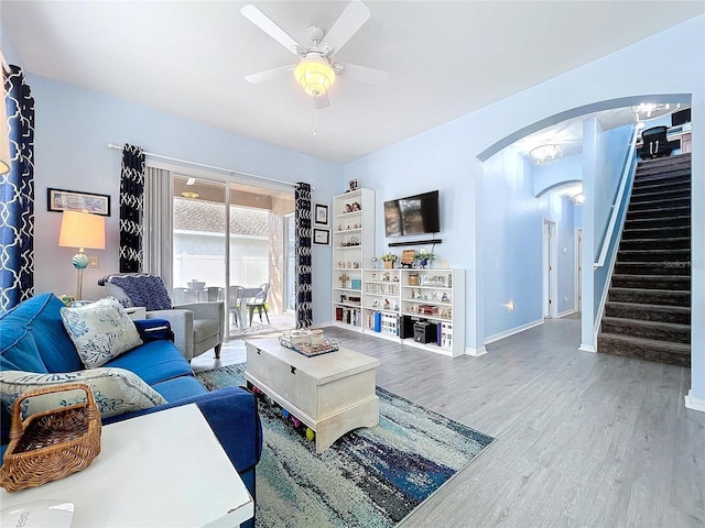 living room with arched walkways, stairway, ceiling fan, wood finished floors, and baseboards