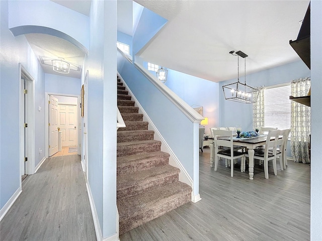 stairway with a healthy amount of sunlight, a notable chandelier, baseboards, and wood finished floors