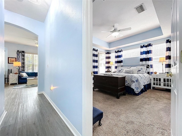 bedroom with arched walkways, a tray ceiling, visible vents, wood finished floors, and baseboards