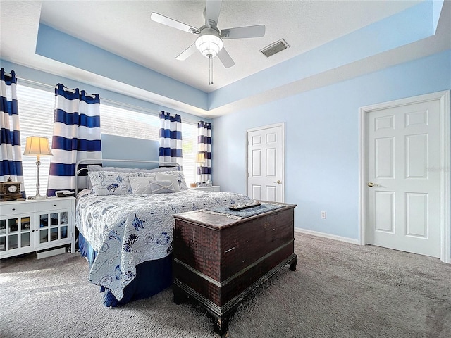 bedroom featuring carpet floors, a ceiling fan, visible vents, baseboards, and a tray ceiling