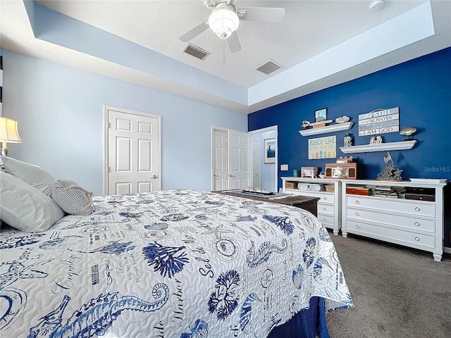 bedroom with ceiling fan, dark carpet, a raised ceiling, and visible vents