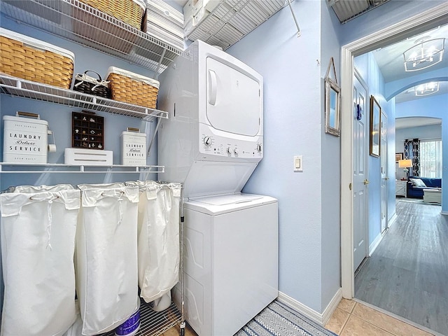 clothes washing area featuring laundry area, stacked washer and dryer, arched walkways, baseboards, and tile patterned flooring