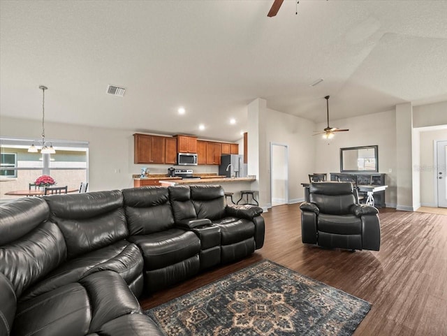 living area featuring visible vents, vaulted ceiling, wood finished floors, baseboards, and ceiling fan with notable chandelier