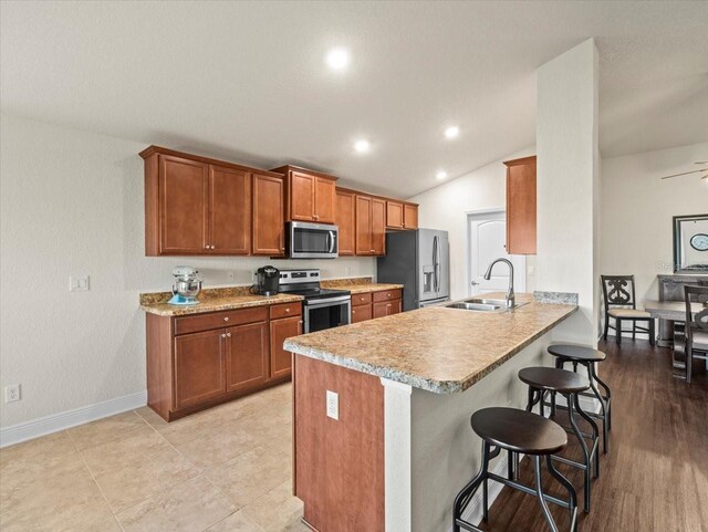 kitchen featuring brown cabinets, stainless steel appliances, a sink, a peninsula, and a kitchen breakfast bar